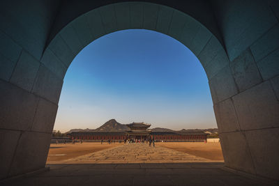 People visiting temple against clear blue sky seen through tunnel