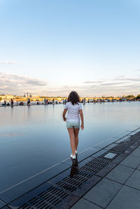 Rear view of teenage girl walking in city against sky