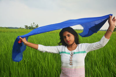 Portrait of young woman with arms raised standing on field