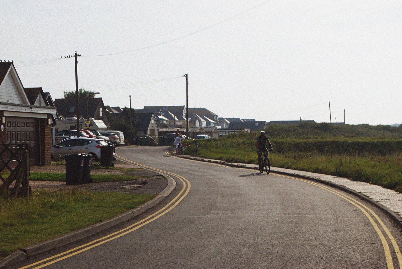 MAN RIDING BICYCLE BY ROAD AGAINST CLEAR SKY