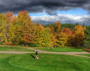 People walking on grassy field against cloudy sky