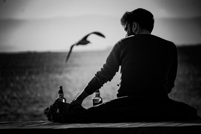 Rear view of man having alcohol while sitting by sea