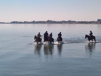 People sitting on lake against clear sky