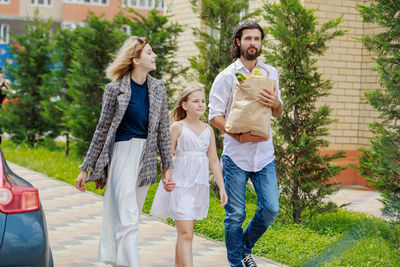 Man with shopping bag by family on footpath against plants