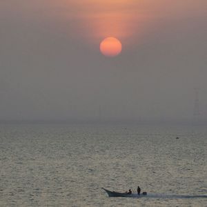 Silhouette people in sea against sky during sunset