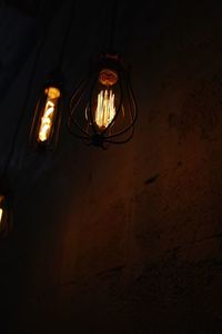 Low angle view of illuminated light bulb hanging on wall