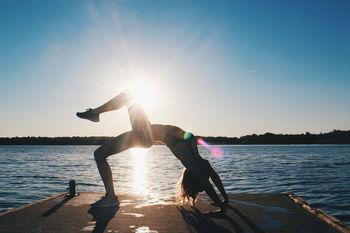 Young woman exercising on beach against clear sky