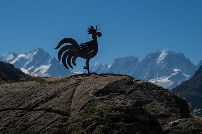 Metallic rooster sculpture on rock against mountain