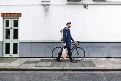 Man with bag of oranges wheeling with bicycle on footpath