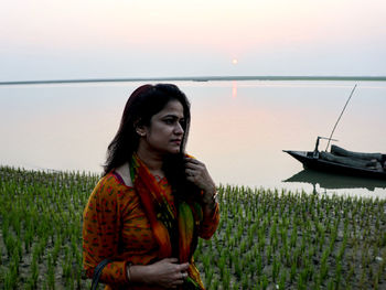 Young woman standing on field against sky during sunset