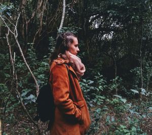 Young woman looking away while standing on tree in forest