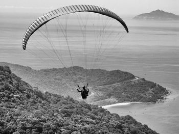 Rear view of man paragliding above mountains against sea