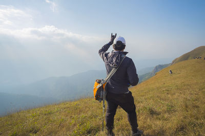 Rear view of hiker showing horn sign on mountain against sky