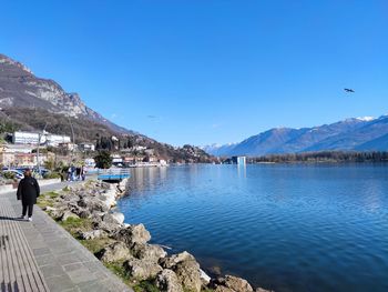 People on lake by mountains against clear blue sky