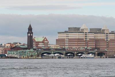 View of buildings by river against cloudy sky