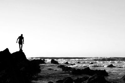 Silhouette man standing on rock by sea against clear sky