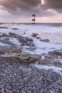 Lighthouse by sea against sky during sunset