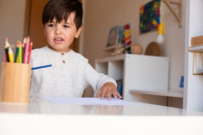 Happy boy holding colored pencil at home