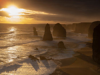 Rocks on beach against sky during sunset