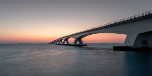 Bridge over sea against sky during sunset