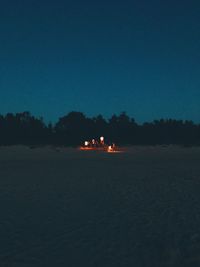 Silhouette people on illuminated land against clear blue sky at night