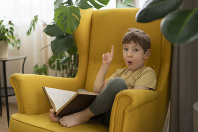 Portrait of cute boy sitting on sofa at home