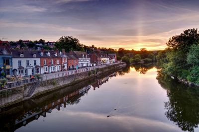 Scenic view of river by buildings against sky at sunset