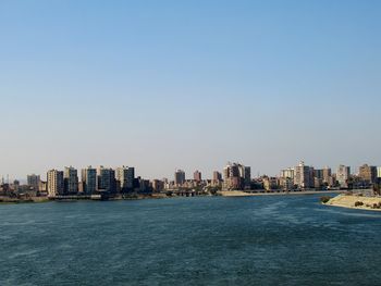 City buildings by sea against blue sky