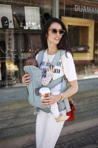 Woman carrying baby walking against store