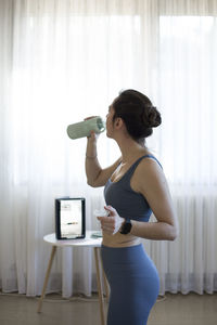 Side view of a young woman drinking water at home