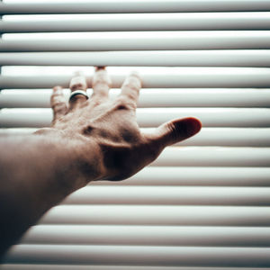 Cropped hand reaching through window blinds