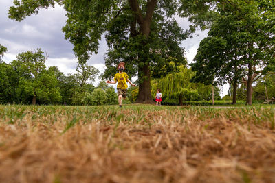 Children running on field by trees against sky