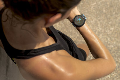 From above of crop anonymous sweaty female runner checking pulse on fitness tracker during workout on sunny day in summer