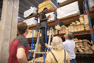 Saleswoman standing on ladder gesturing while talking with customers at hardware store