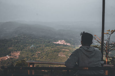 Rear view of man looking at cityscape against sky