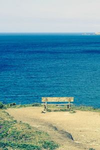 Empty bench on shore by sea against sky