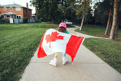 Girl wrapped in large canadian flag riding on roller skates in park. canada day celebration 