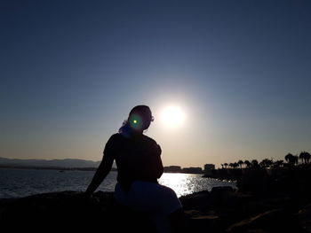 Silhouette man on rock at beach against sky during sunset