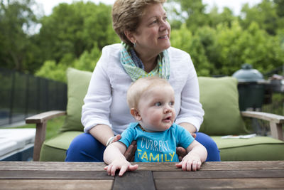 Grandmother looking away while holding grandson at yard