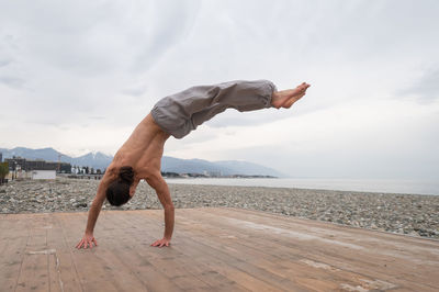 Low section of woman jumping at beach against sky