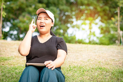 Woman sitting on field against trees