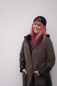 Happy young woman with pink hair standing against white wall