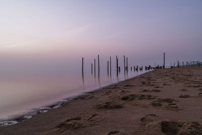 Wooden posts on beach against sky during sunset