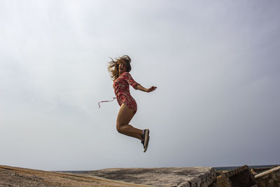 Low angle view of young woman jumping on land against sky