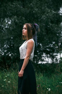 Young woman looking away while standing against trees