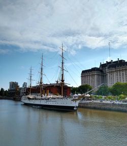 Sailboats in river by buildings against sky