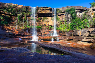 Waterfall falling from mountain top with reflection and blue sky at morning from low angle