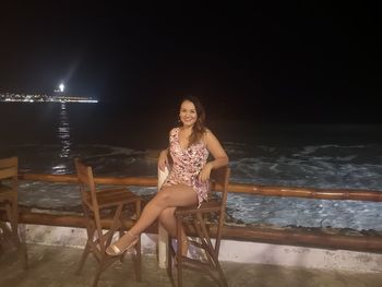 Portrait of woman sitting by sea against sky at night