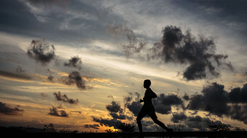 Silhouette boy running against sky during sunset