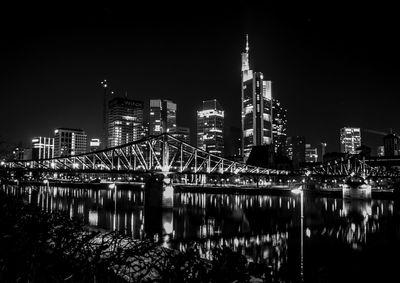 Illuminated bridge over river by buildings against sky at night